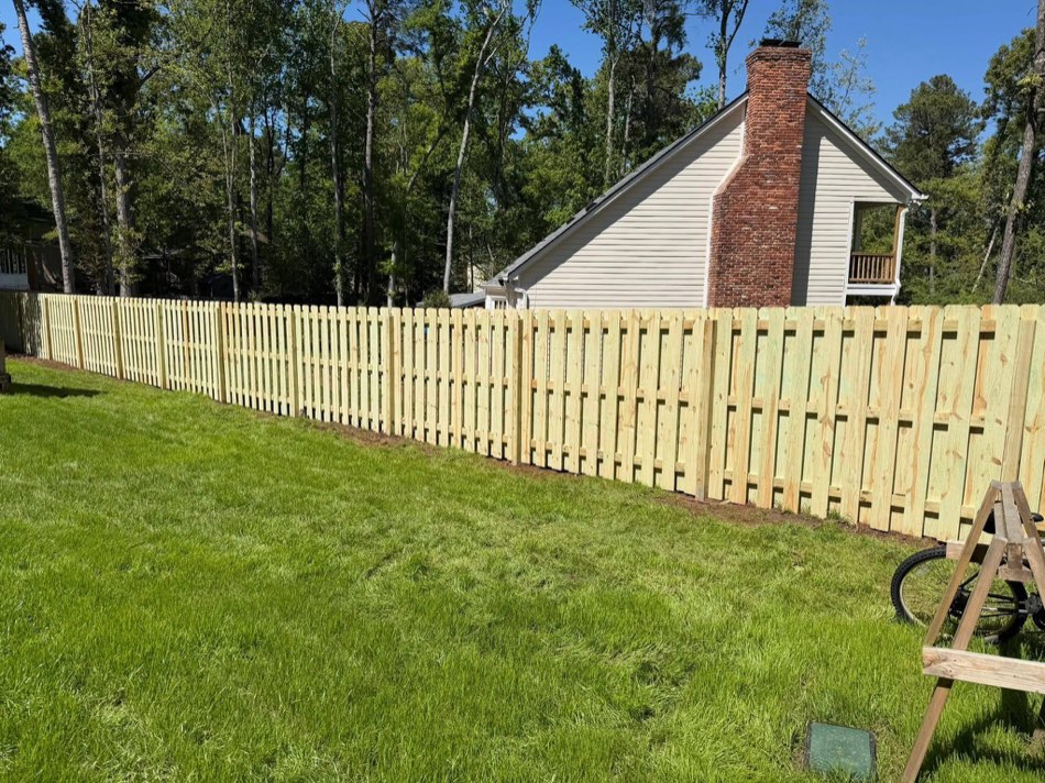 Long shadowbox privacy fence run along a green lawn with white farmhouse