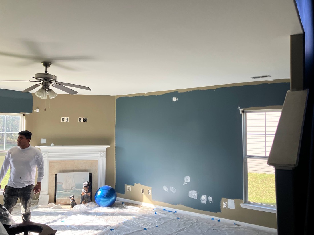 Blue accent wall in progress with painter and fireplace