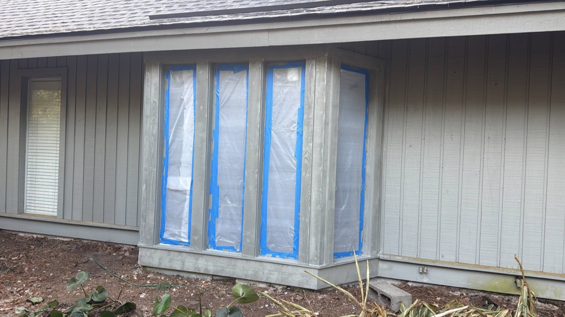 Exterior windows masked with blue tape and plastic before painting